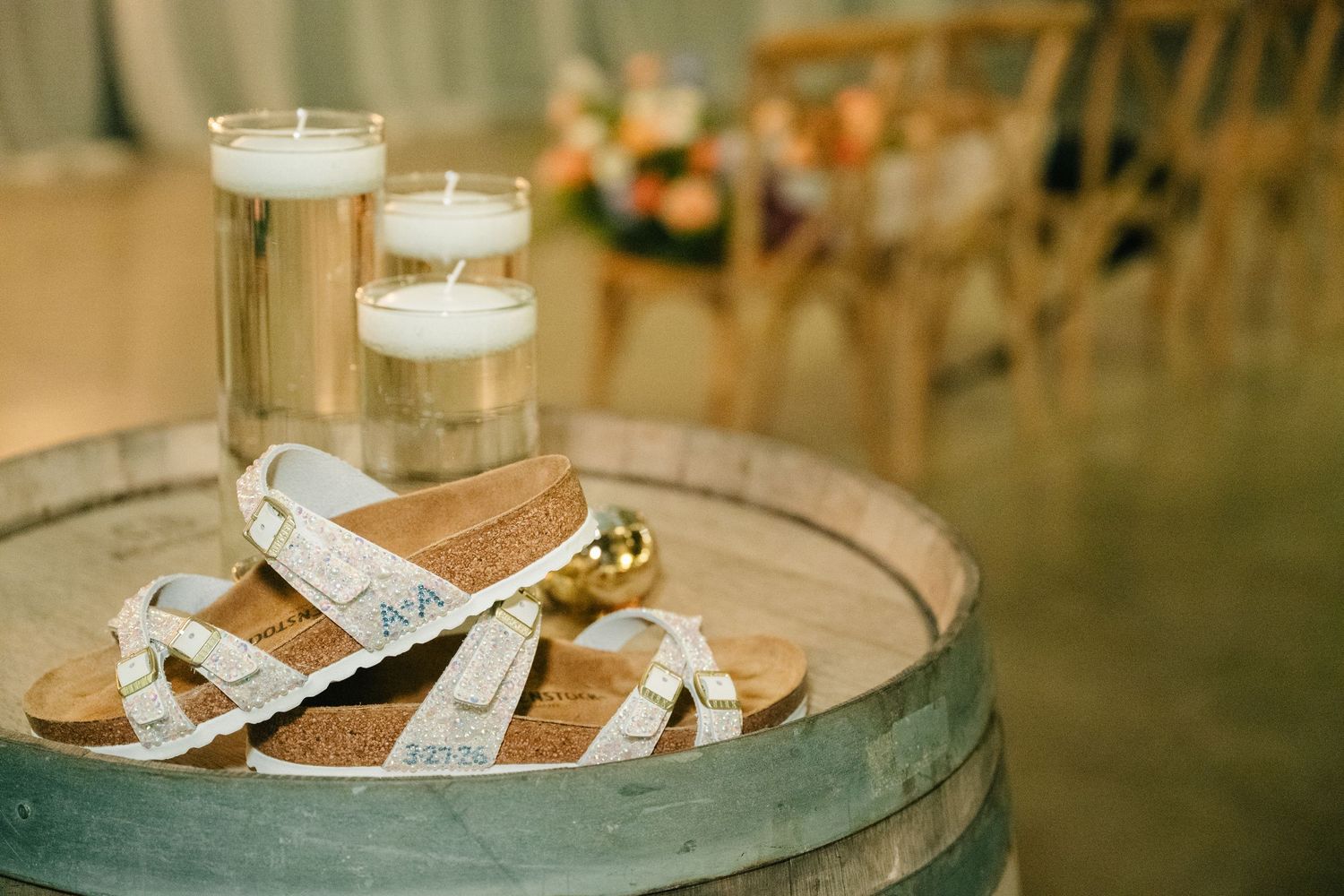 White sandals on a wooden barrel with floating candles at a wedding venue.
