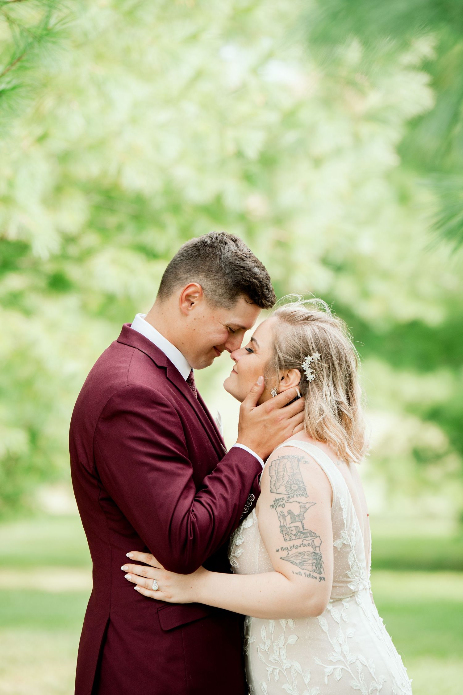 Central MN Wedding Photography - Bride and groom share an intimate moment touching foreheads in a lush green park setting.