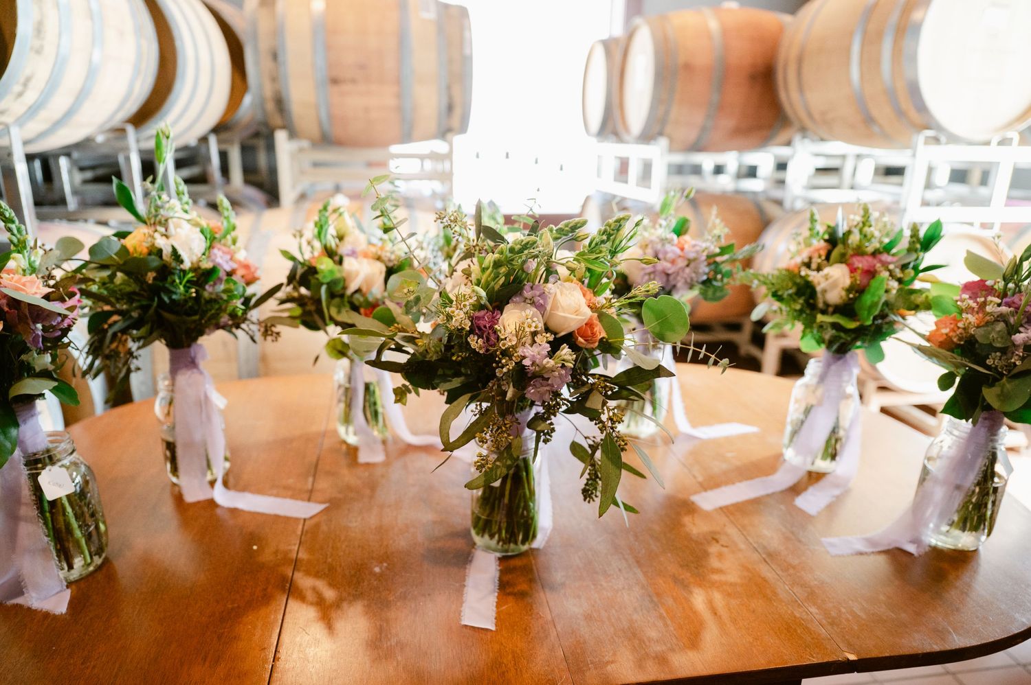Central MN Wedding Photos - Rustic wedding bouquets in mason jars on wooden table with wine barrels in background at winery venue.