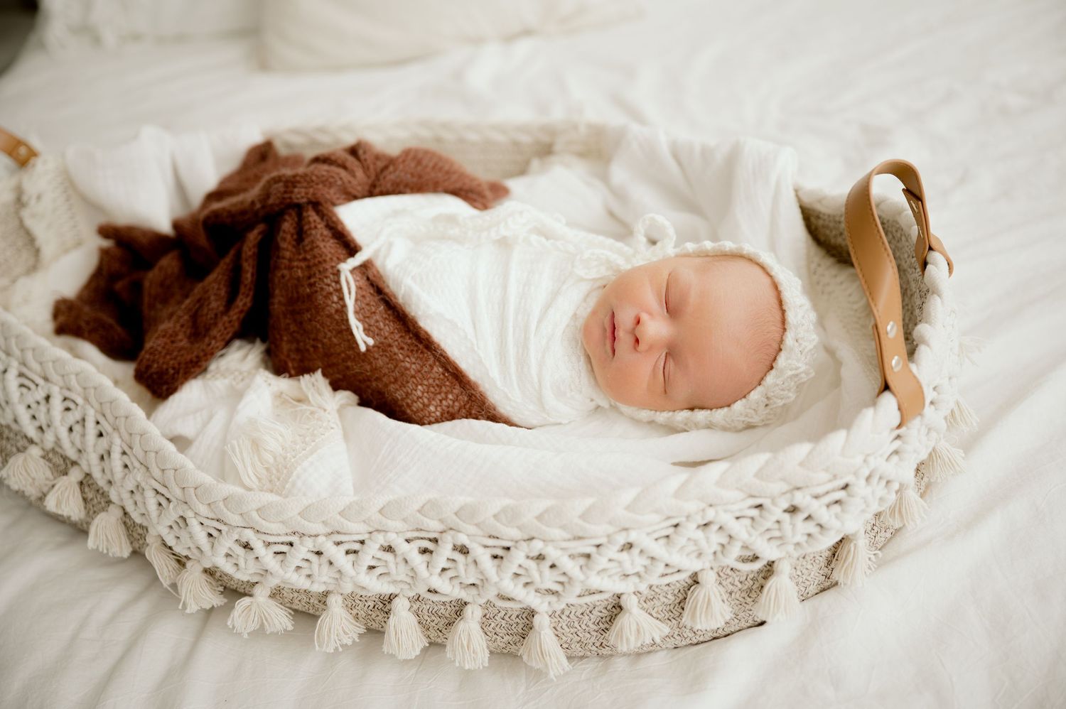Newborn baby sleeping peacefully in a white wicker Moses basket with a brown knit blanket.