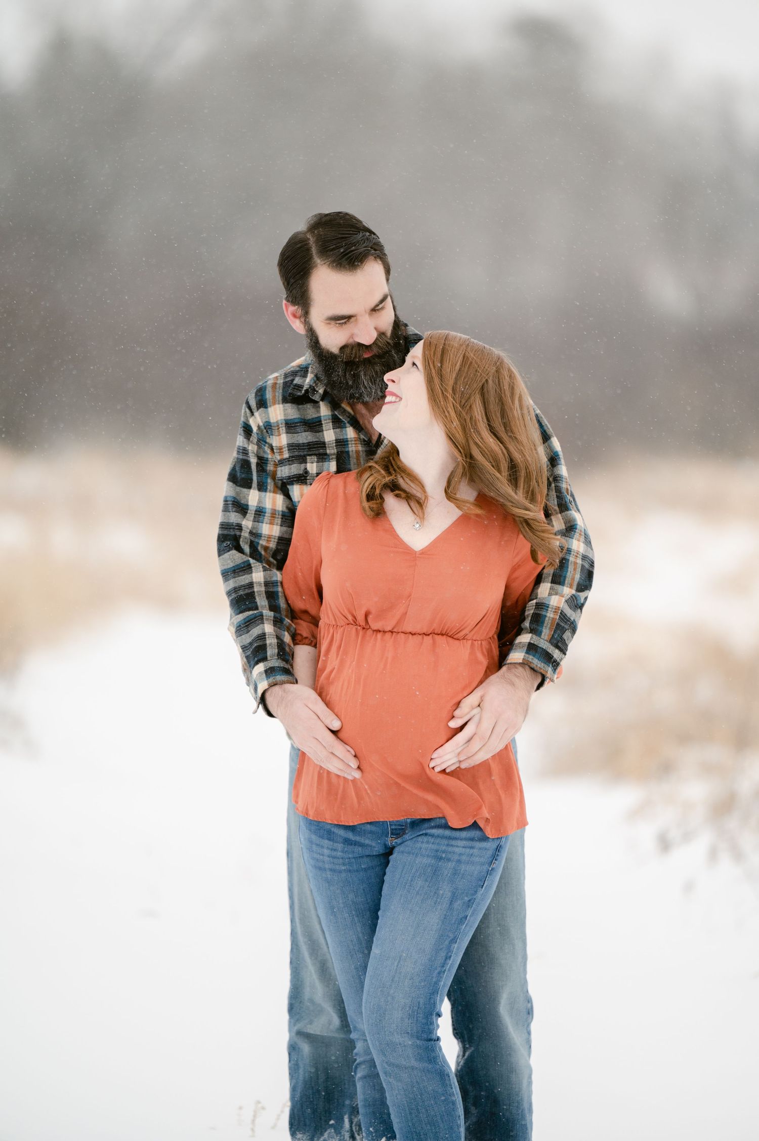 Intimate couple portraits in a snowy setting with the pair wearing plaid and rustic orange casual clothing.