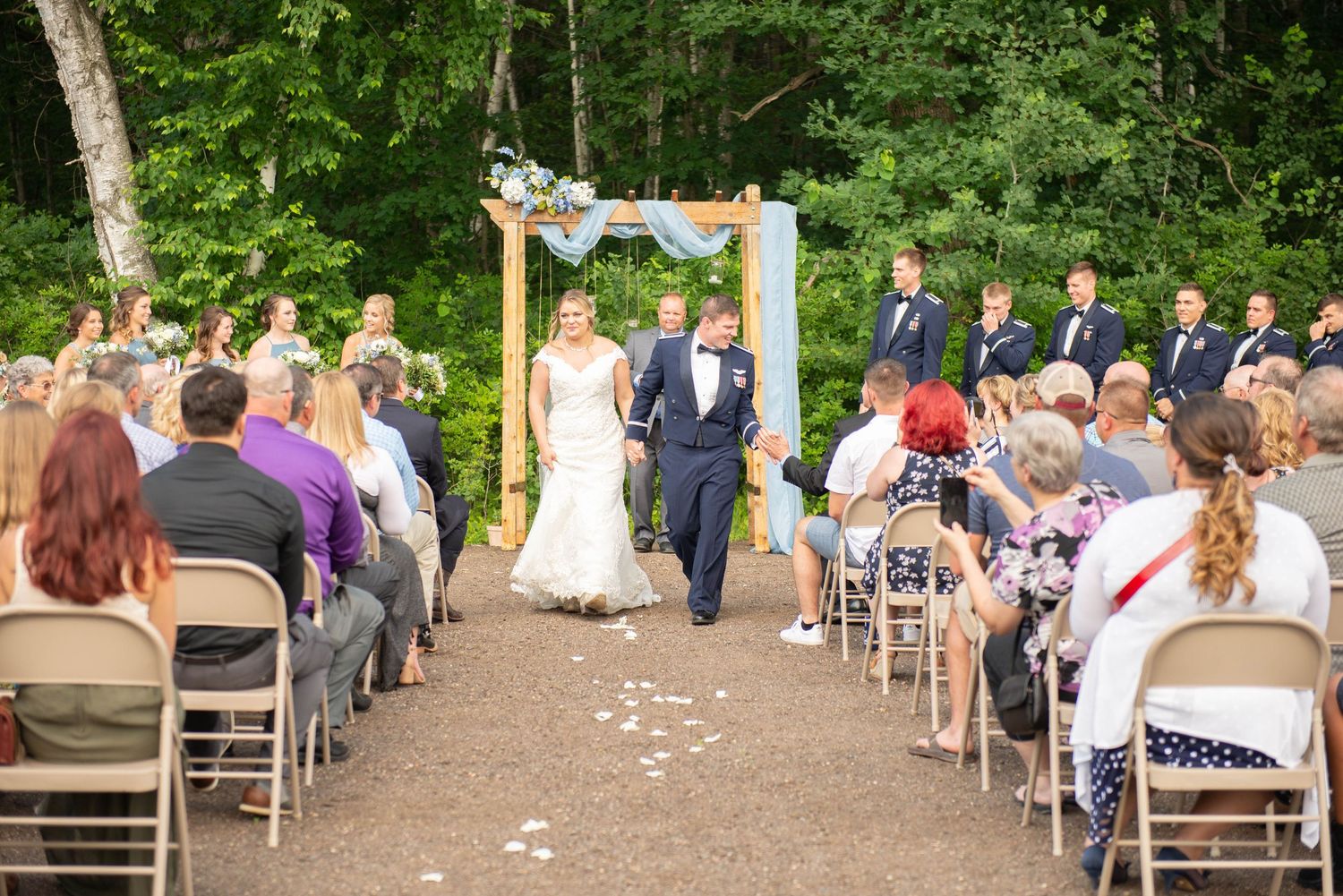 Wedding guests seated on wooden chairs along a gravel pathway during an outdoor ceremony. Zimmerman MN Weddings