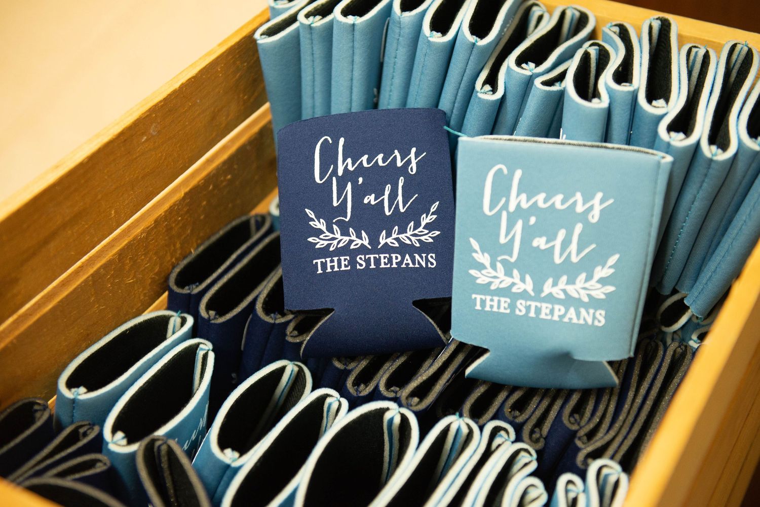 Blue wedding koozies with 'Cheers Y'all' text displayed in a wooden box. Zimmerman MN Weddings