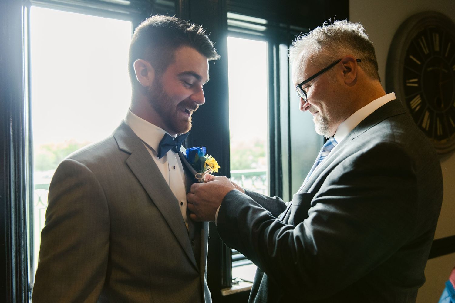Central MN Wedding Photos | Father pins boutonniere on groom wearing gray suit and navy bow tie before wedding ceremony.