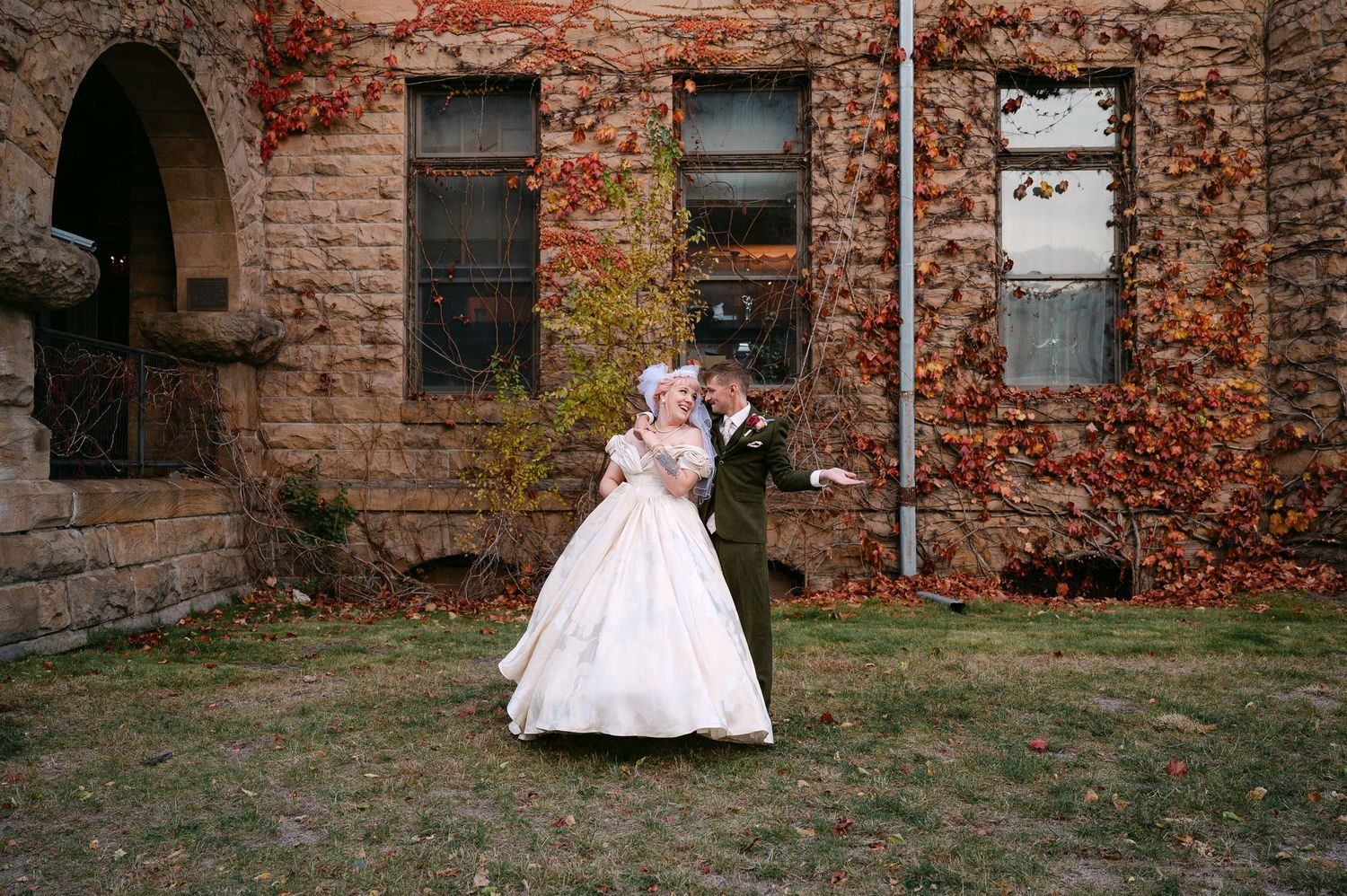 Central MN Wedding Photos | Bride and groom posing before stone building with autumn ivy foliage.