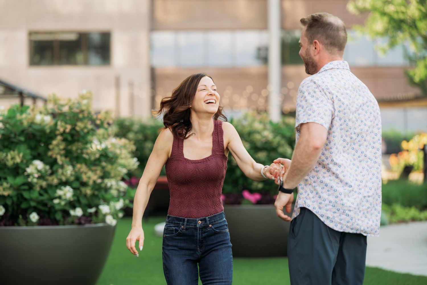 A couple laughs together while dancing in a garden with string lights in the background.