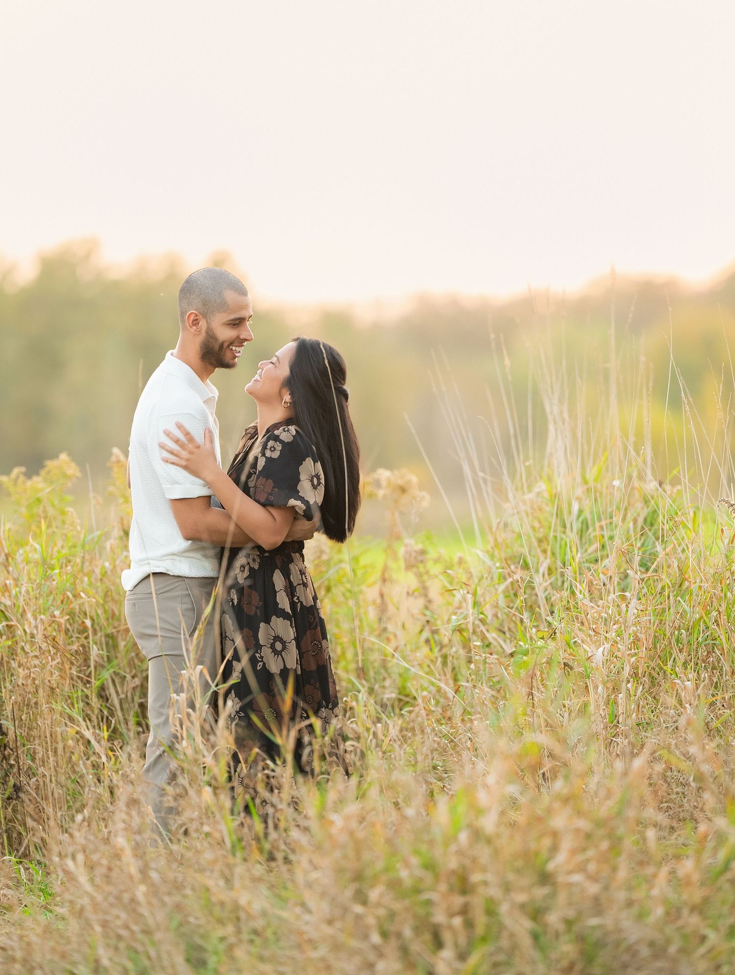 A couple shares an intimate moment together in a sunlit meadow of tall grass during golden hour.