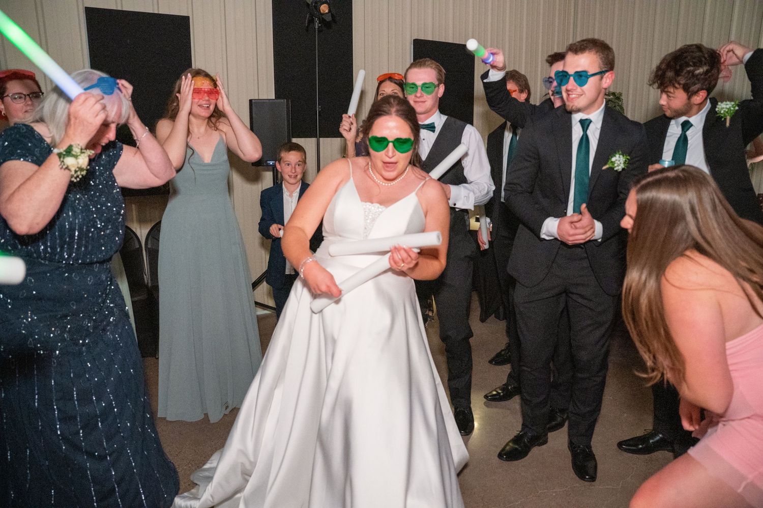 Wedding guests dance and celebrate on a lively reception dance floor with colorful lighting.