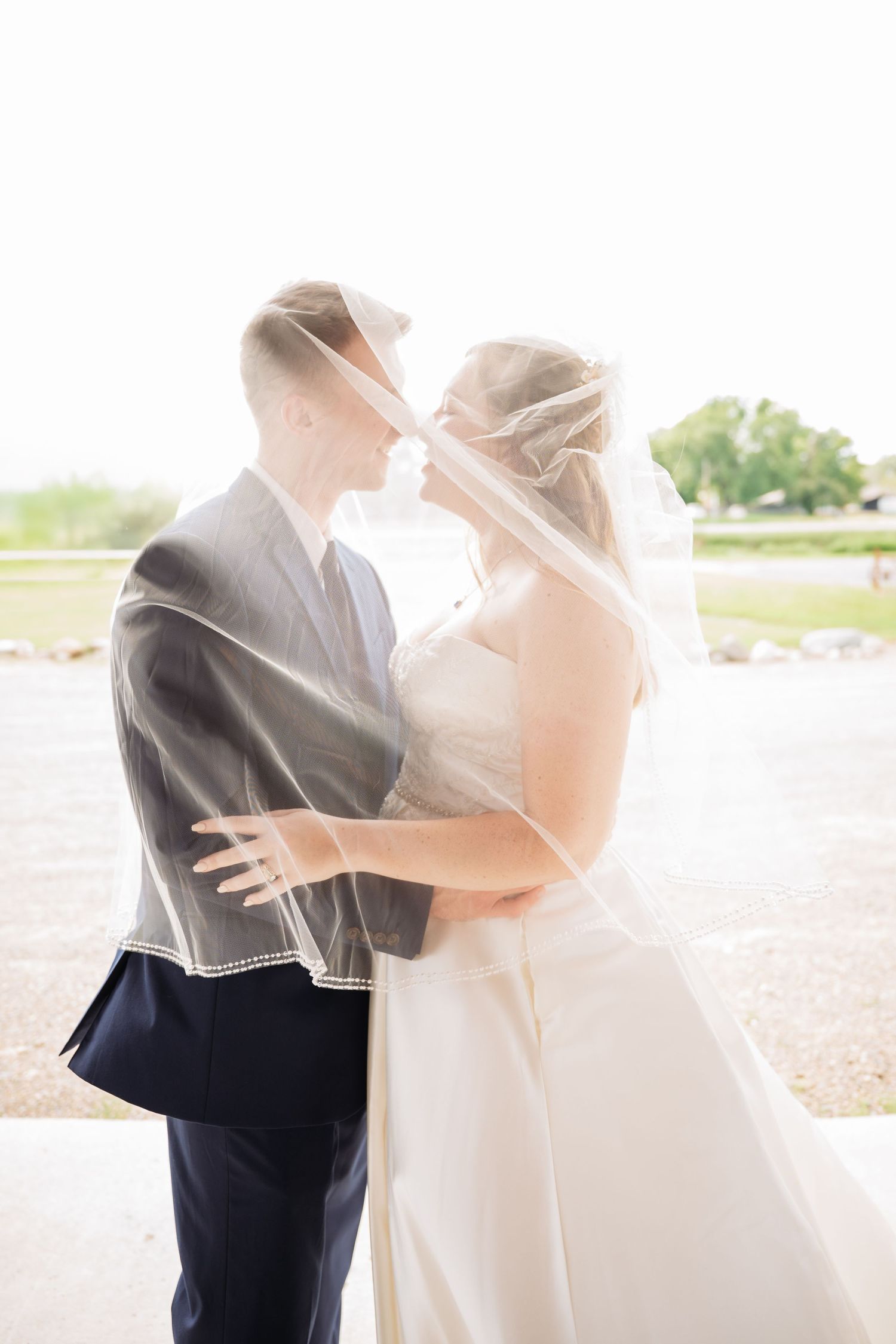 A romantic wedding couple embraces outdoors in a dreamy sunlit setting with flowing veil. Pease Minnesota Wedding at Northern Lights Ballroo