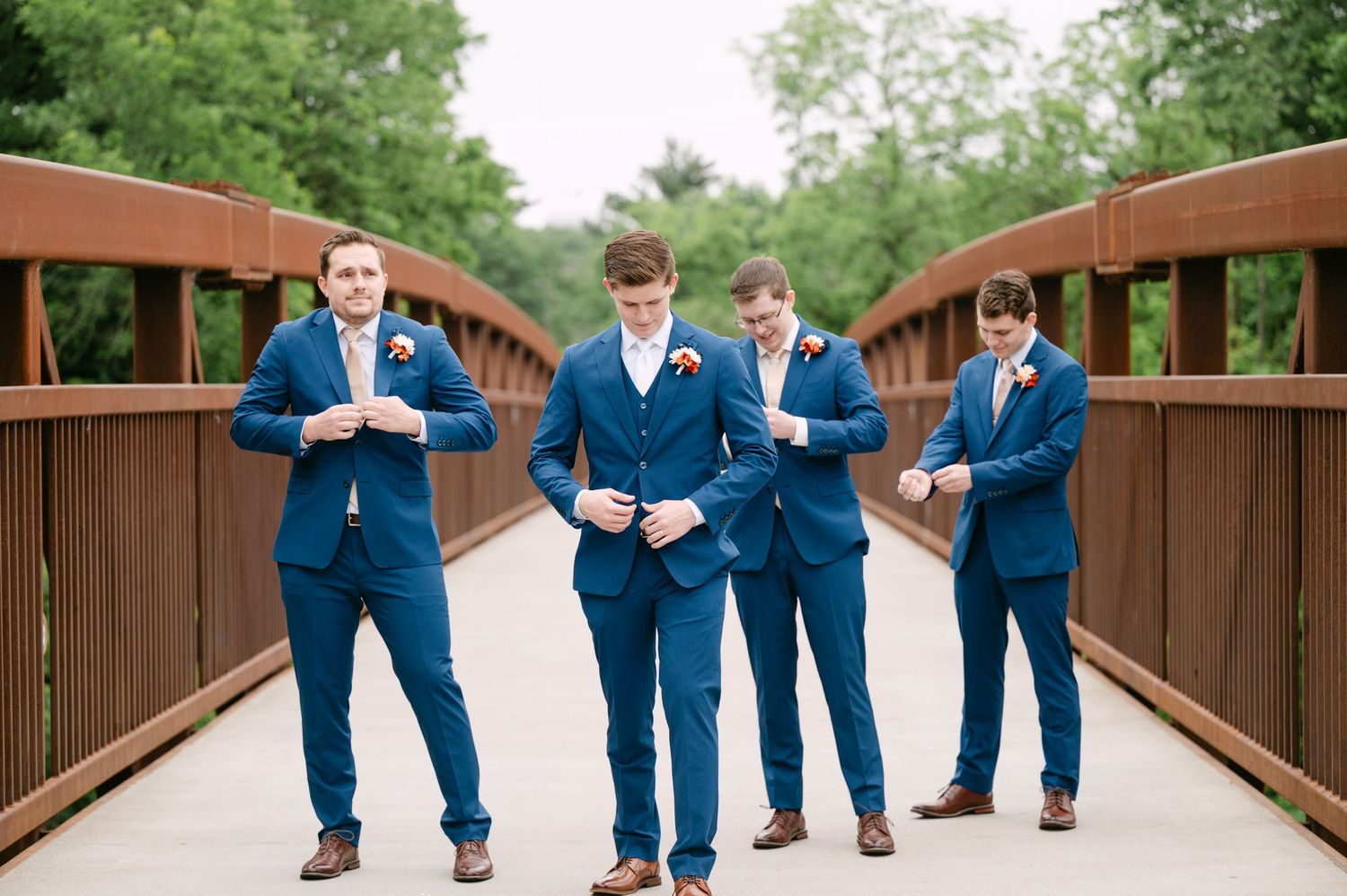 Groomsmen in navy blue suits walking together on a wooden bridge.