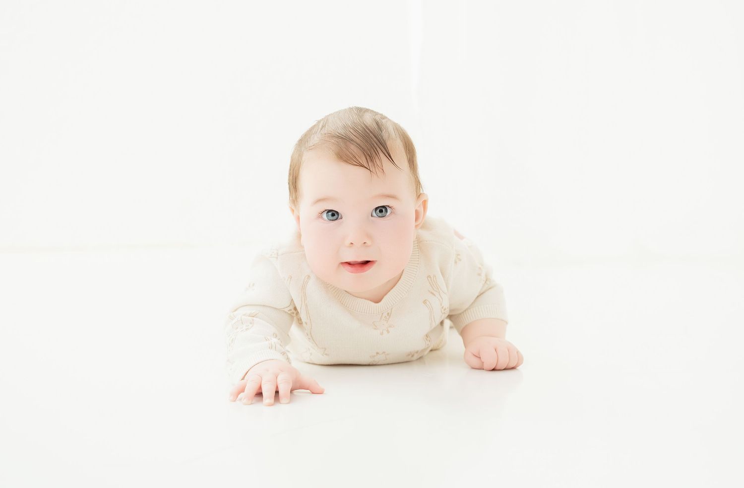 Baby in beige outfit doing tummy time on white surface looking at camera.. Minnesota milestone photographer