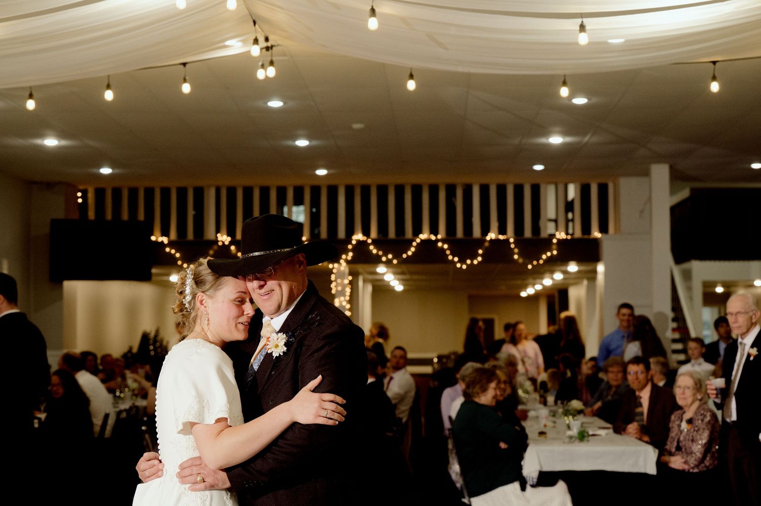 A wedding reception dance captured under warm string lights with guests watching in the background.