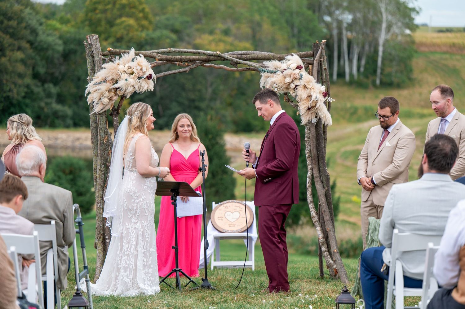 Rustic outdoor wedding ceremony under a floral arch with dried pampas grass decorations.