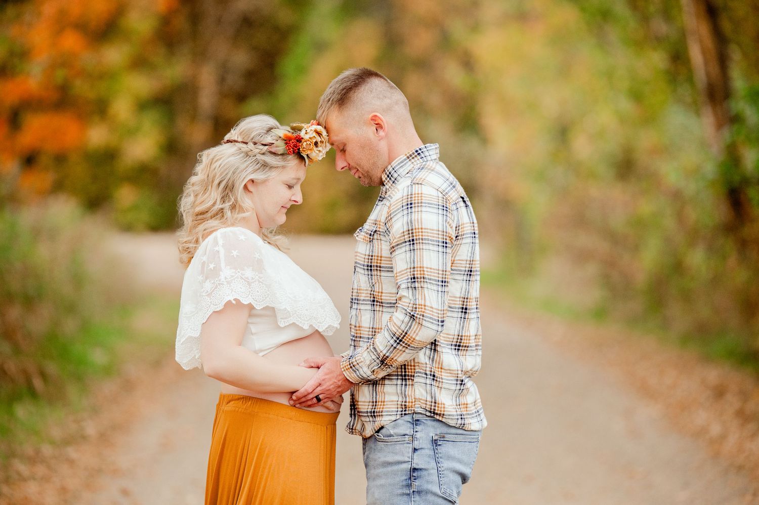 Two people share a romantic embrace on a path surrounded by autumn foliage and golden light.