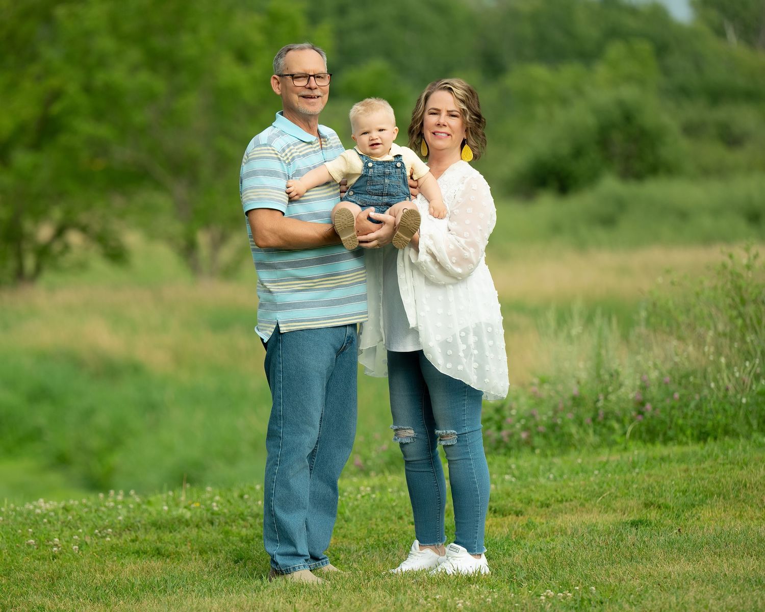 Family group in casual attire stands together on lush green grass for outdoor summer portrait session. Family Portraits & Milestone Moments