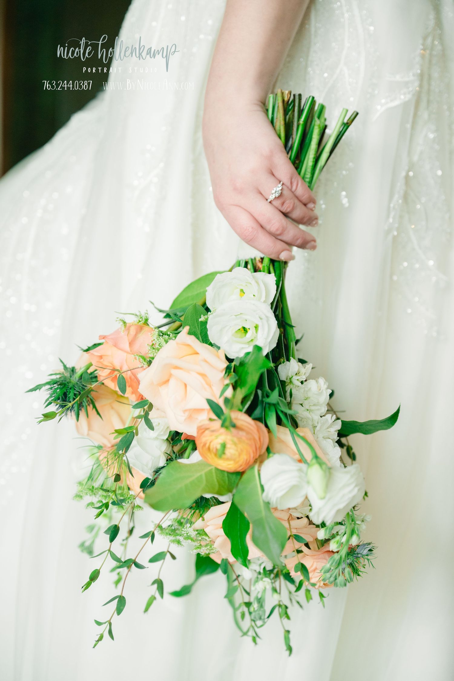 A delicate bridal bouquet featuring peach ranunculus, white roses and fresh greenery against a white lace dress.
