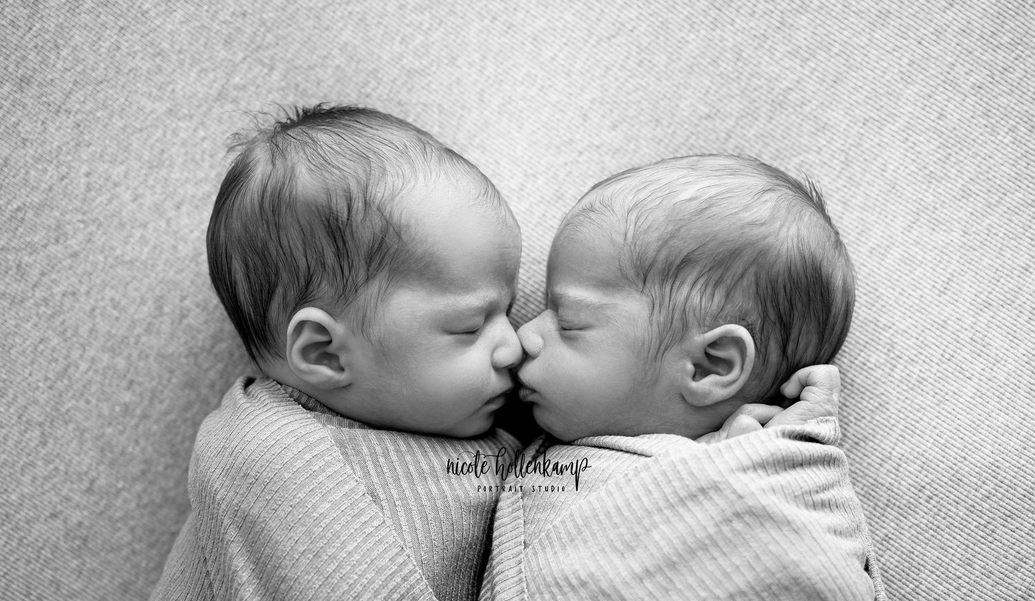 Black and white portrait of twin infants lying close together in matching outfits.