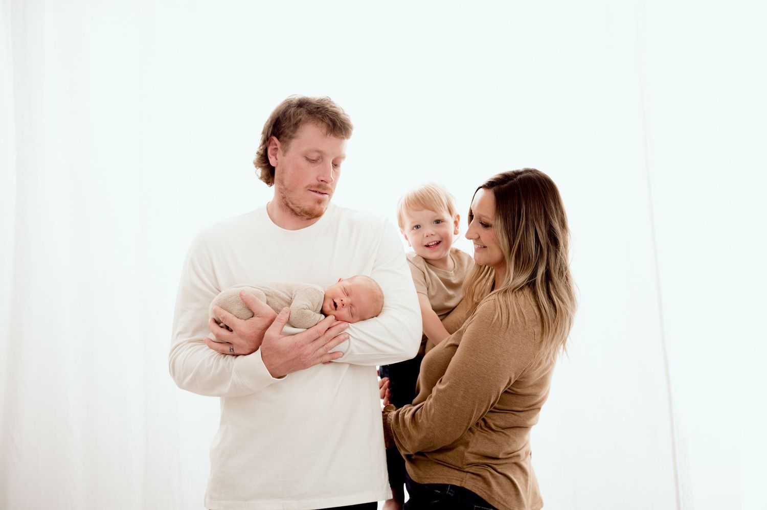St Cloud newborn Photos of A family of four with parents holding a newborn and toddler against a white background.