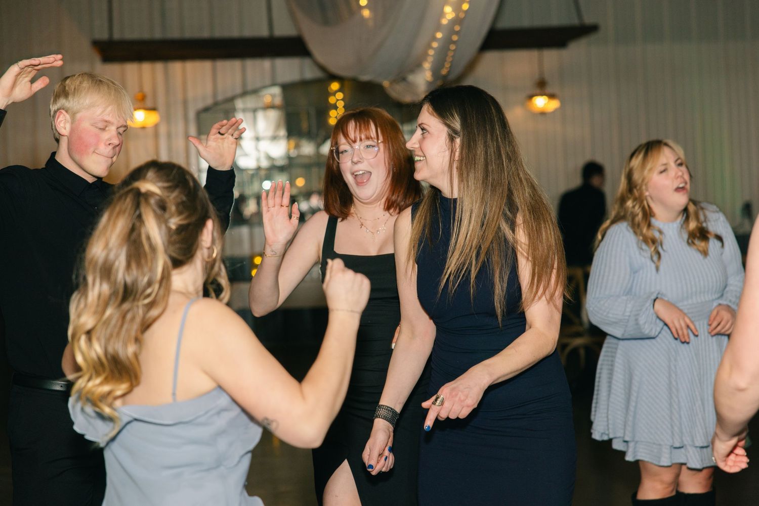 Wedding guests dancing and laughing joyfully on the dance floor during evening reception celebration.