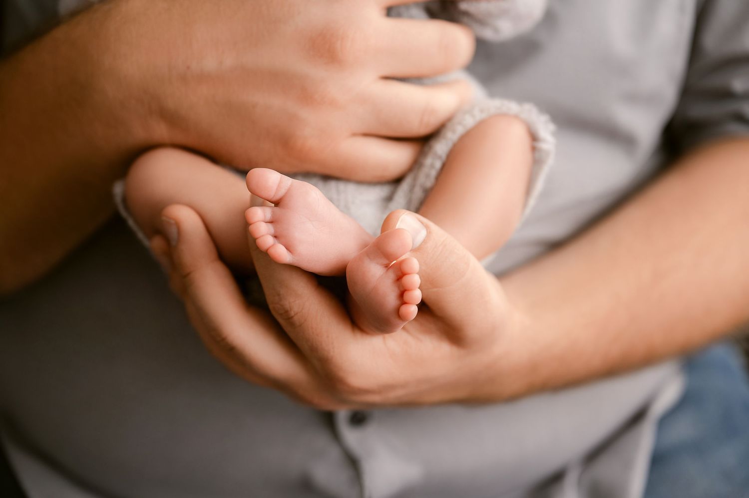 St Cloud newborn Photos of Adult hands gently cradling tiny newborn baby feet against a gray shirt.