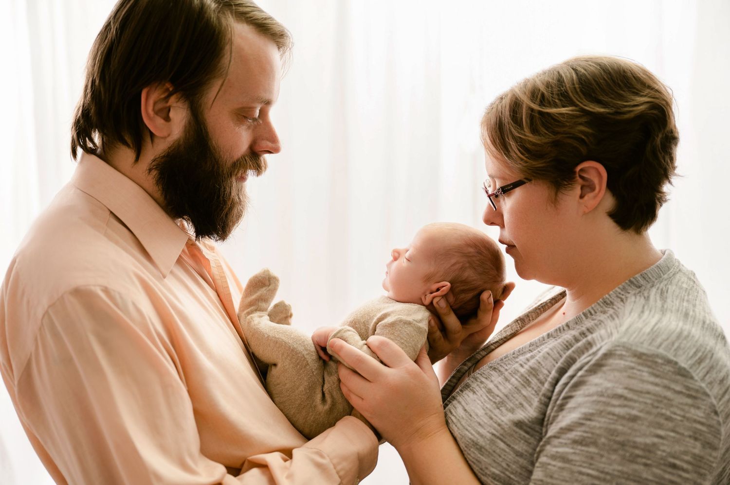A tender moment between parent and newborn baby showing physical connection and nurturing care in a sunny room.