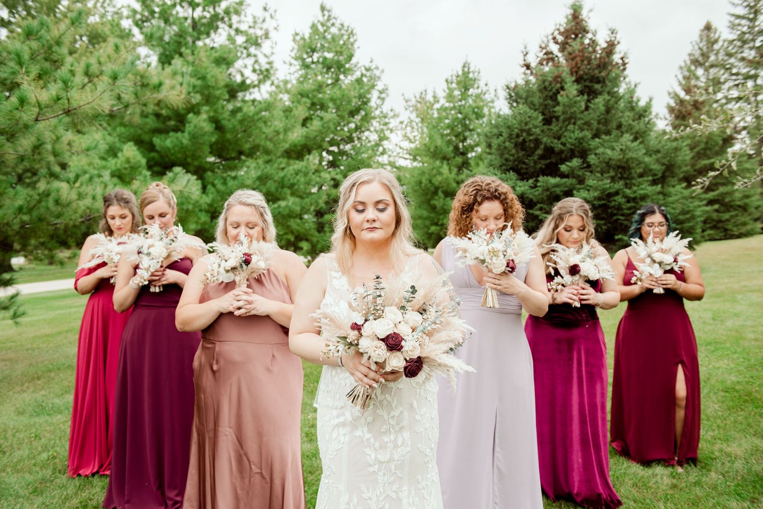 Wedding party in burgundy and blush dresses holding bouquets outdoors.