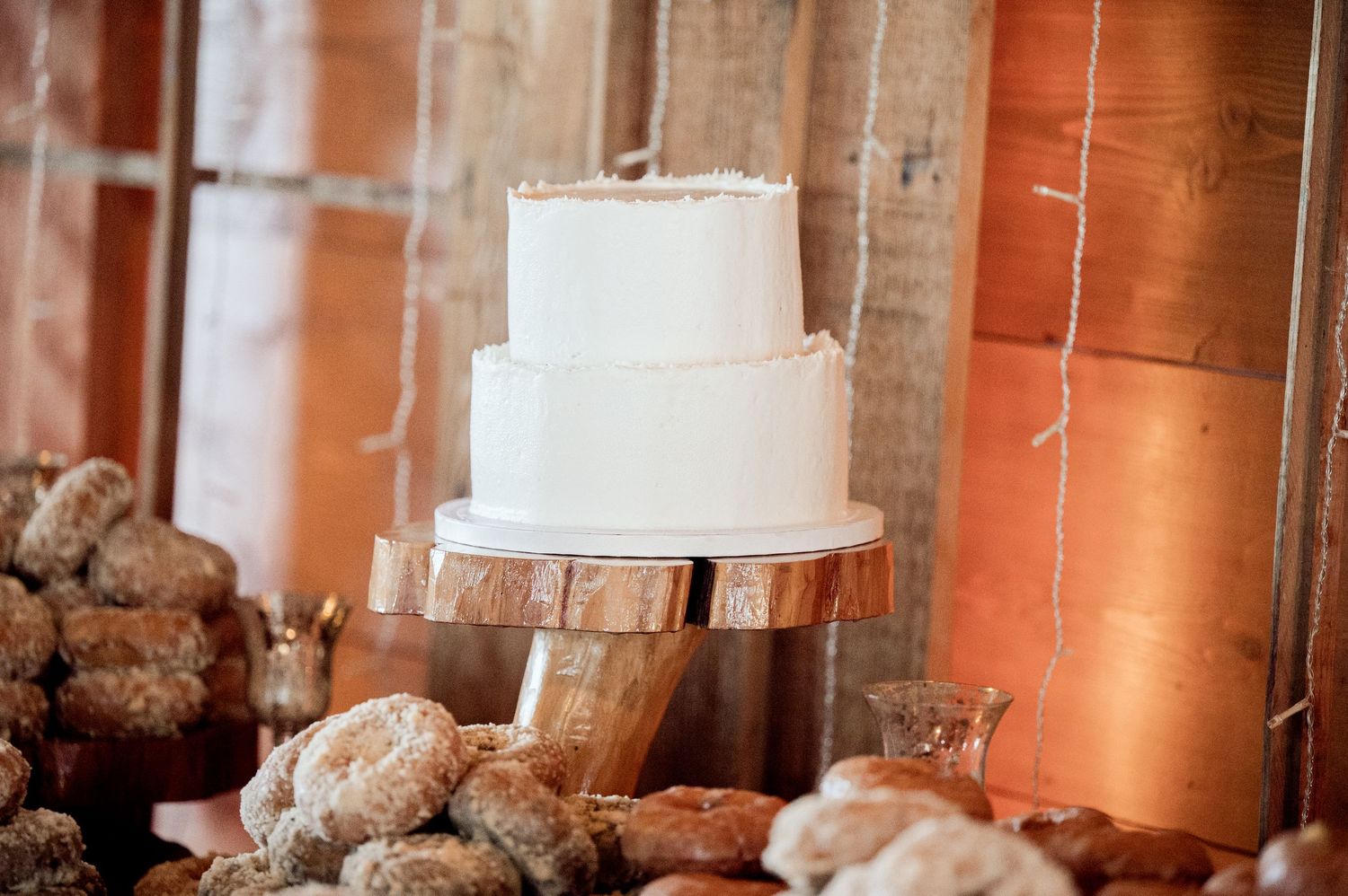 White wedding cake displayed in a barn venue with warm lighting and rustic decor.