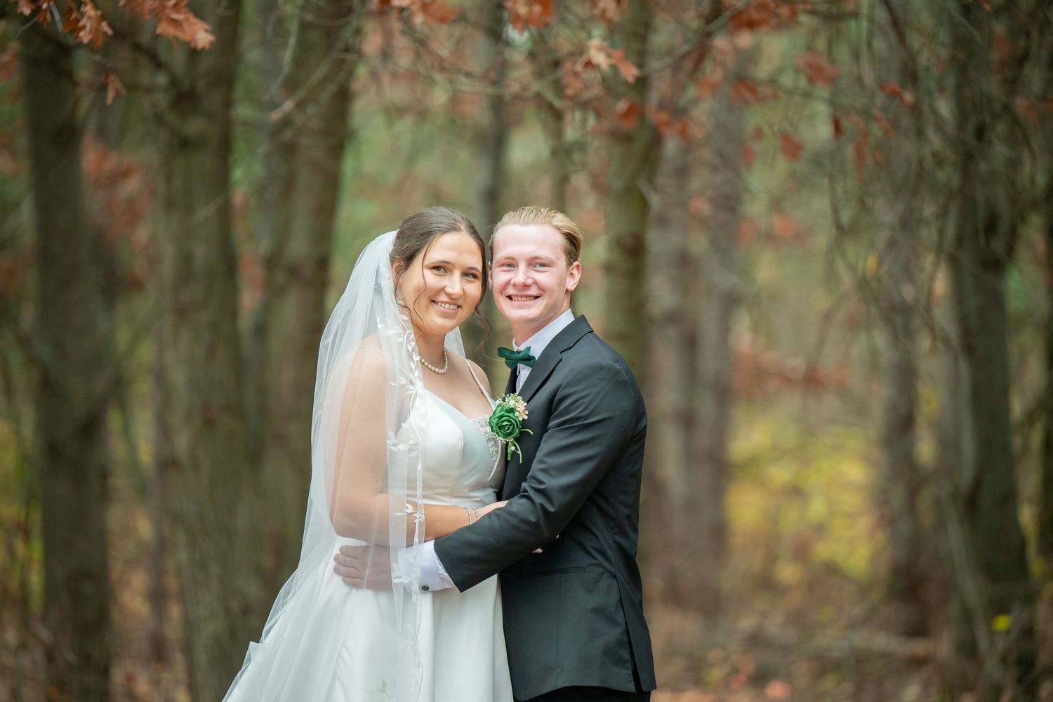 A couple shares a romantic moment in a forest with autumn foliage creating a warm, natural backdrop.