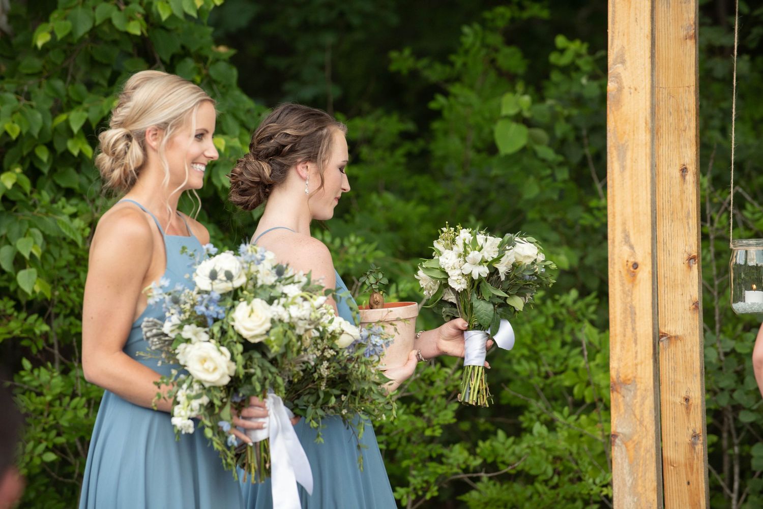 Bridesmaids in light blue dresses hold white and blue floral bouquets during outdoor ceremony. Zimmerman MN Weddings
