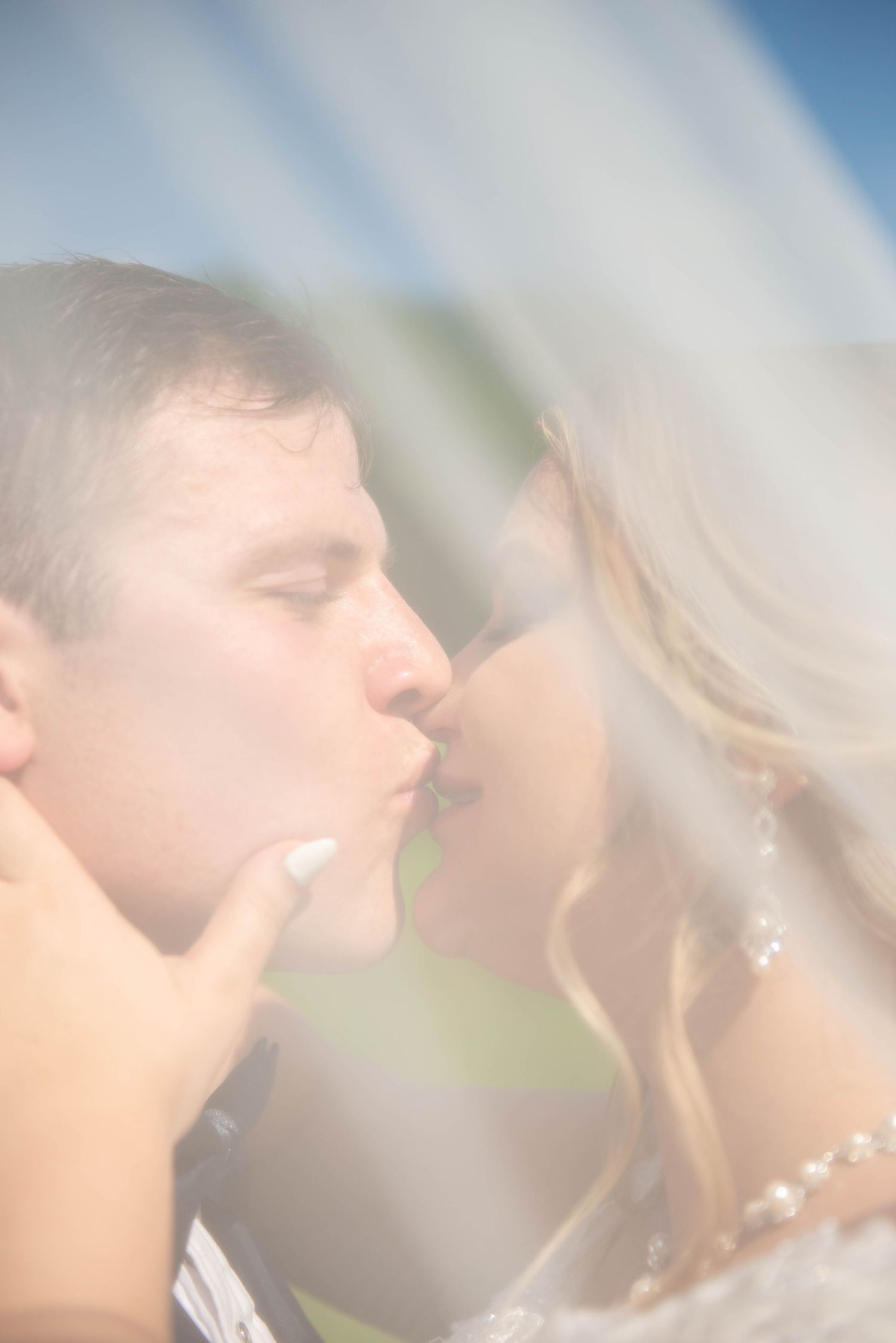 Soft focus romantic wedding kiss captured through dreamy veil effect outdoors. Zimmerman MN Weddings