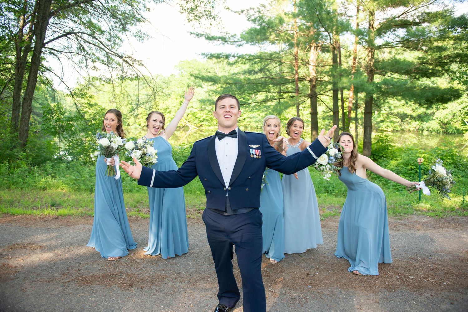 Wedding party in blue attire celebrating with fun poses in forest setting. Zimmerman MN Weddings
