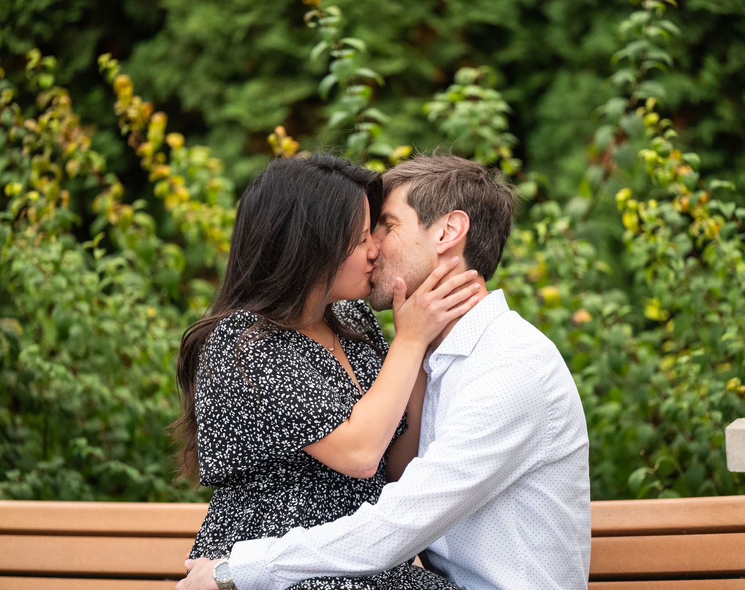 In central Minnesota a couple embracing on a wooden bench surrounded by yellow flowers and greenery.