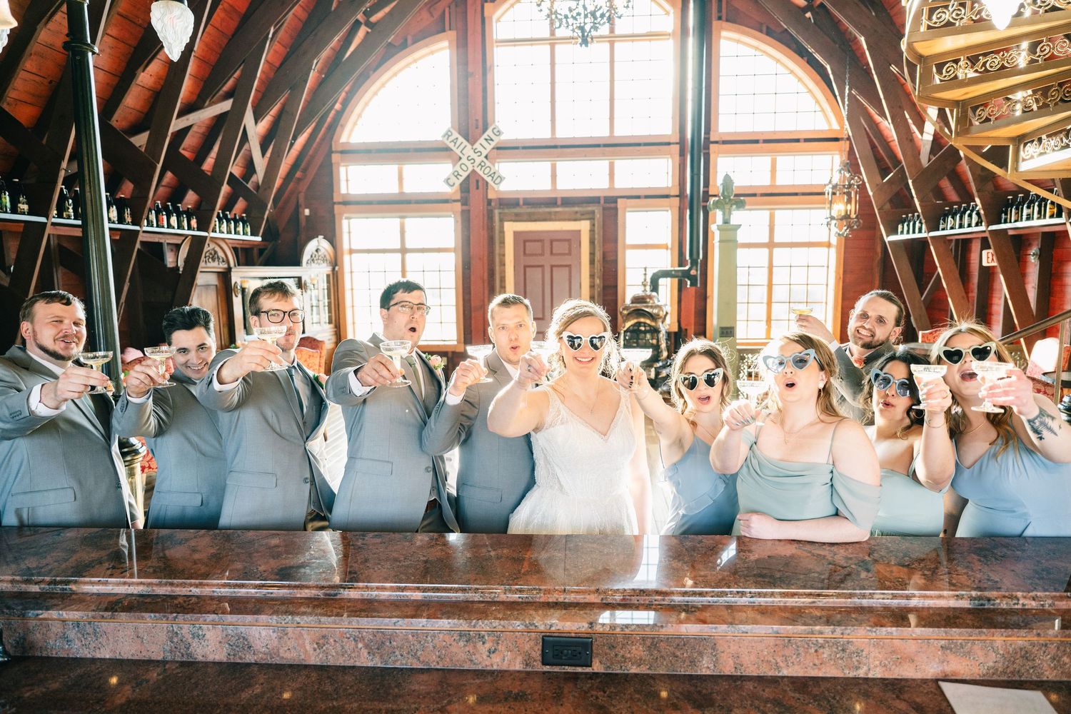 Wedding party posing with fun sunglasses props at a rustic bar venue.