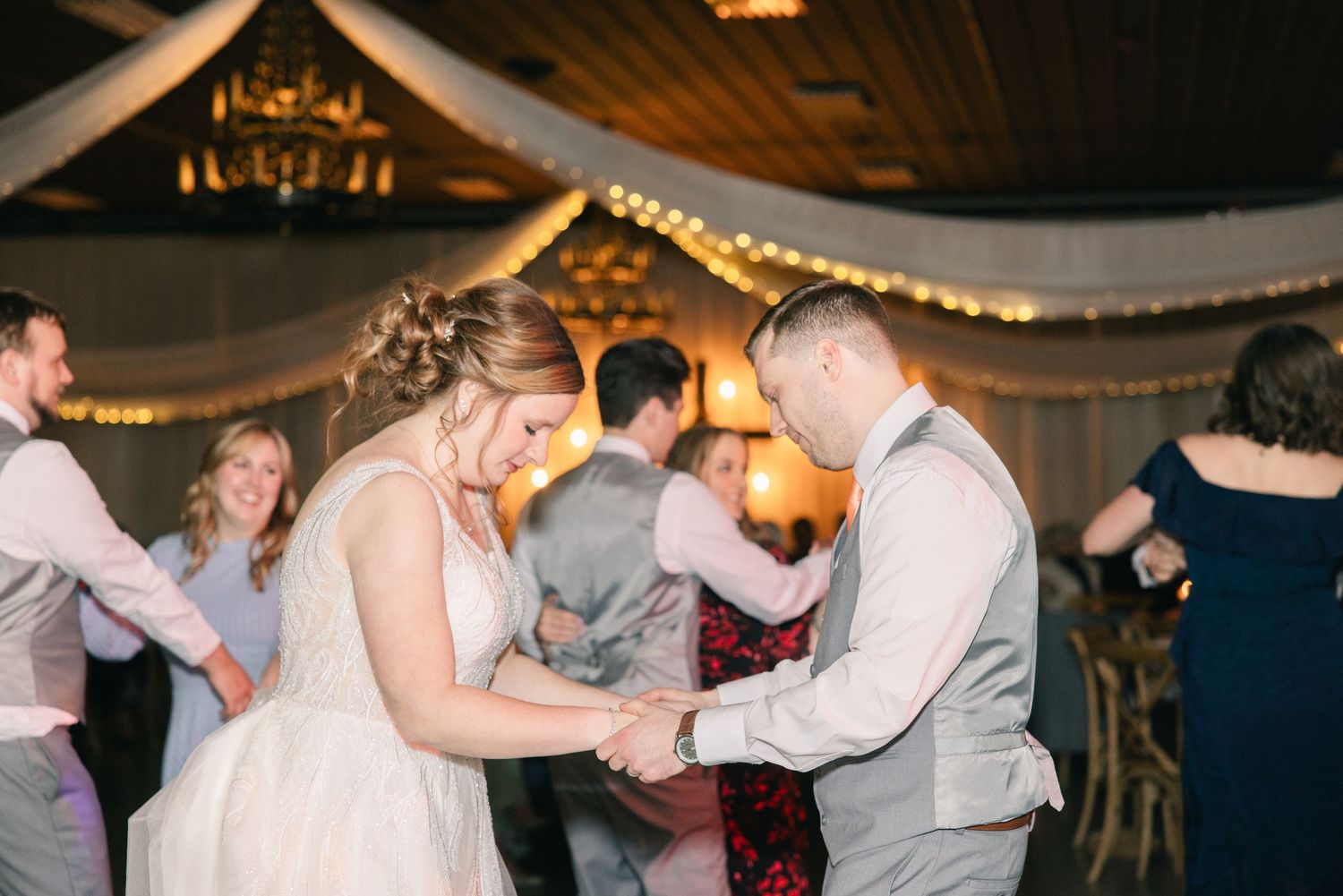 Bride and groom share a joyful dance together surrounded by guests at their wedding reception.