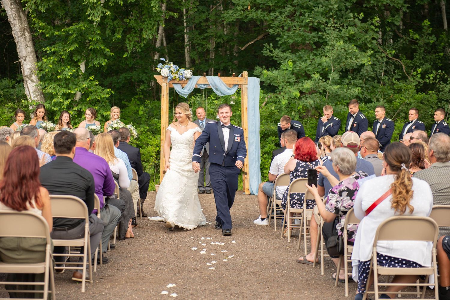 Guests seated on folding chairs at an outdoor wedding ceremony surrounded by trees. Zimmerman MN Weddings