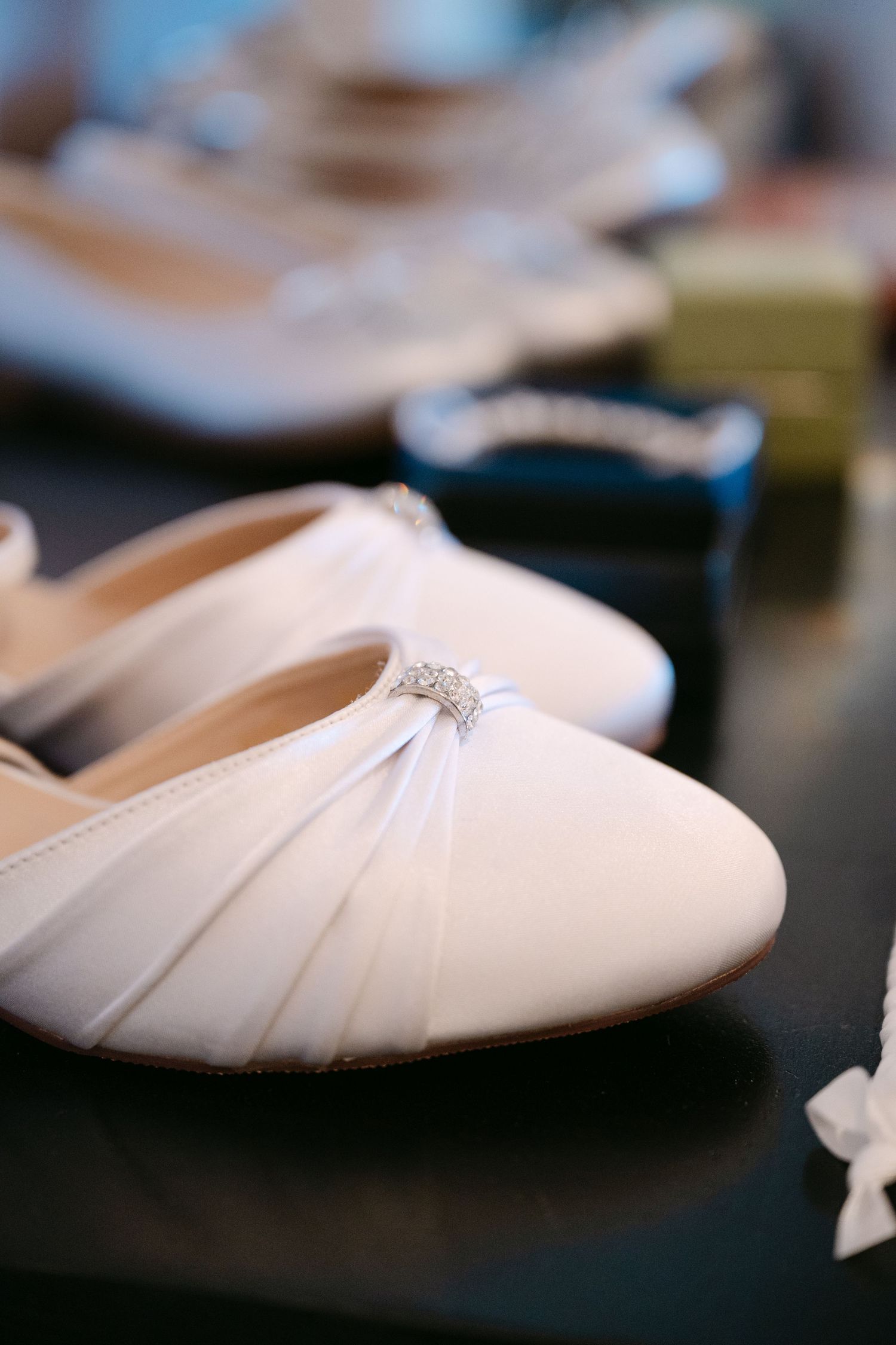 Elegant white satin bridal shoes with pleated details and delicate fabric texture displayed in soft focus.