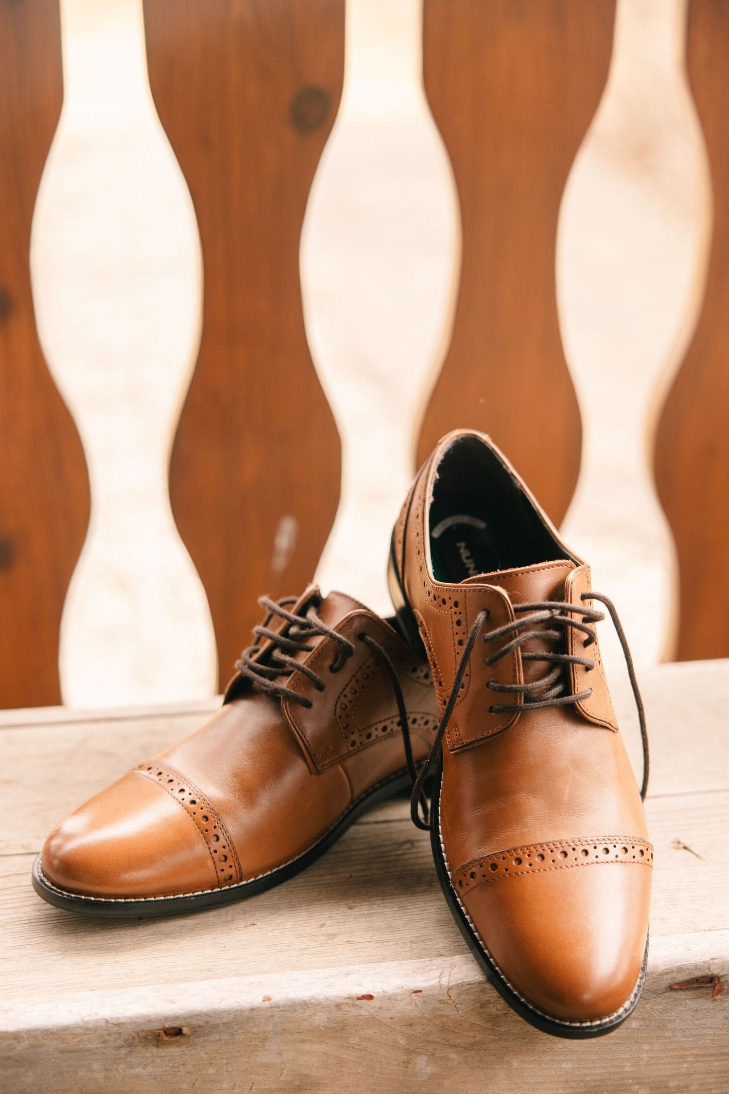 Classic tan leather brogue oxford dress shoes displayed on a wooden surface for a wedding.