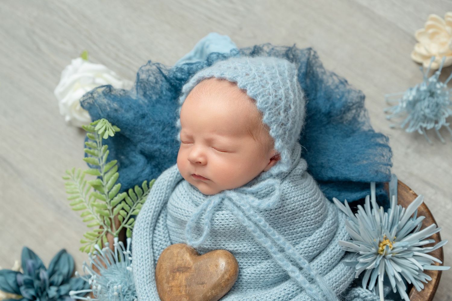 In central MN a Newborn photography setup with soft blue knit blankets, decorative flowers, and rustic wooden props arranged artistically.