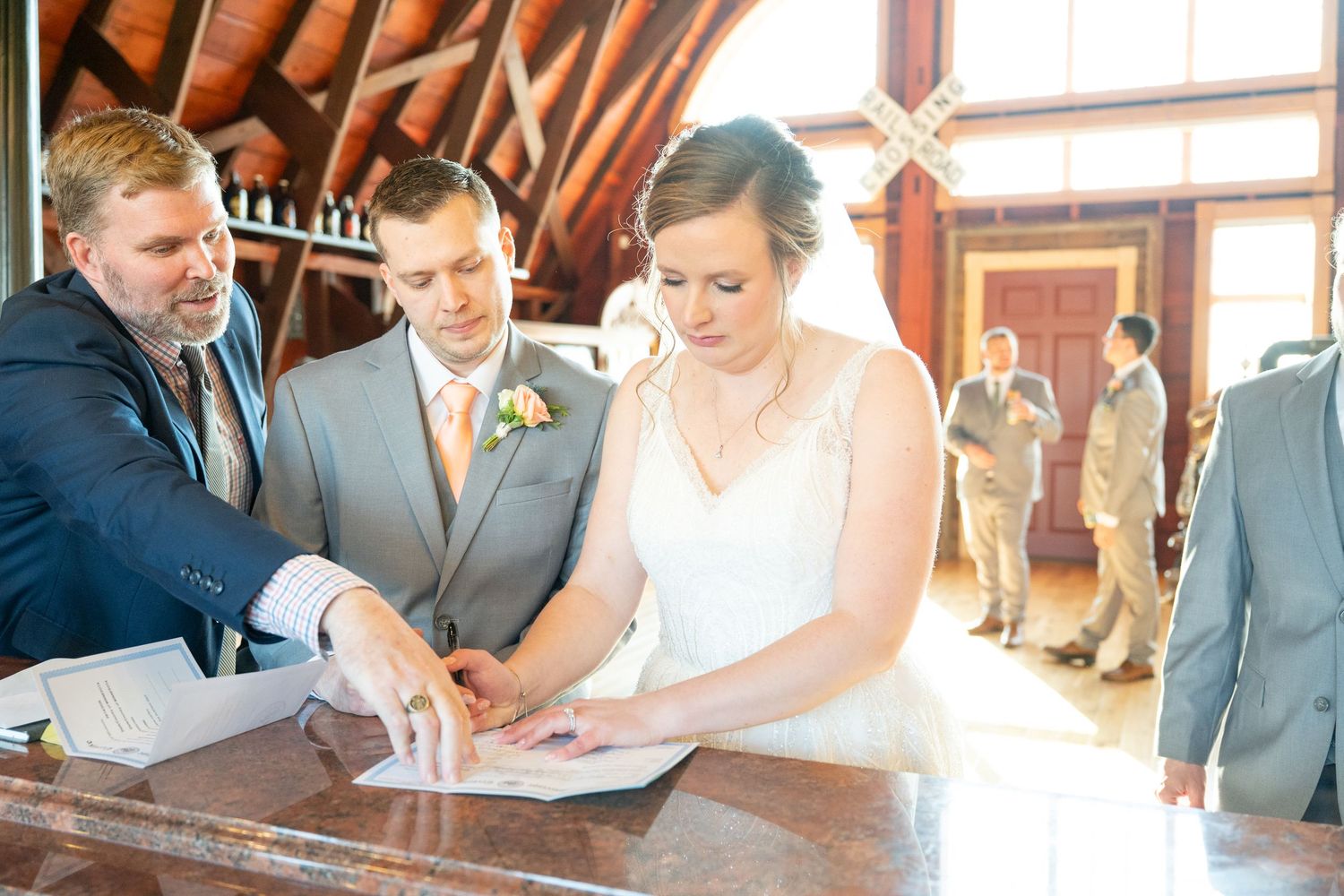 Bride and groom signing marriage certificate at rustic wooden venue.