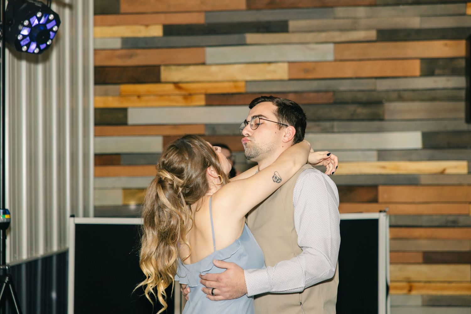 Couple sharing a romantic slow dance in front of a rustic reclaimed wood wall at reception.