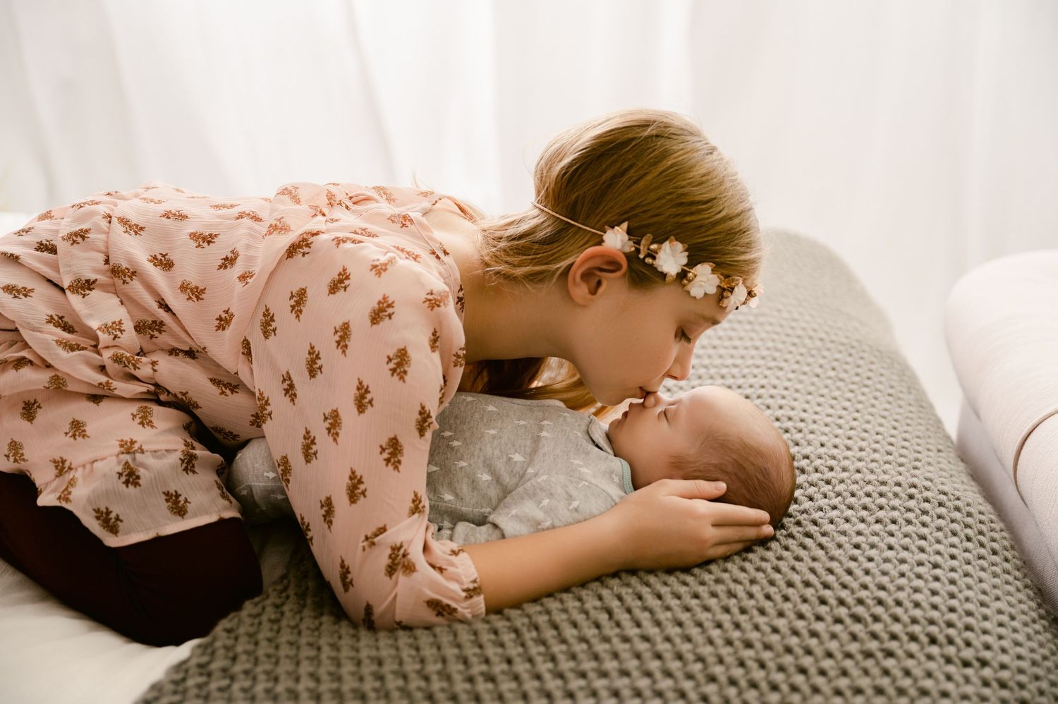 A ruffled pink dress sleeve delicately rests against a knitted gray textile in soft natural light.