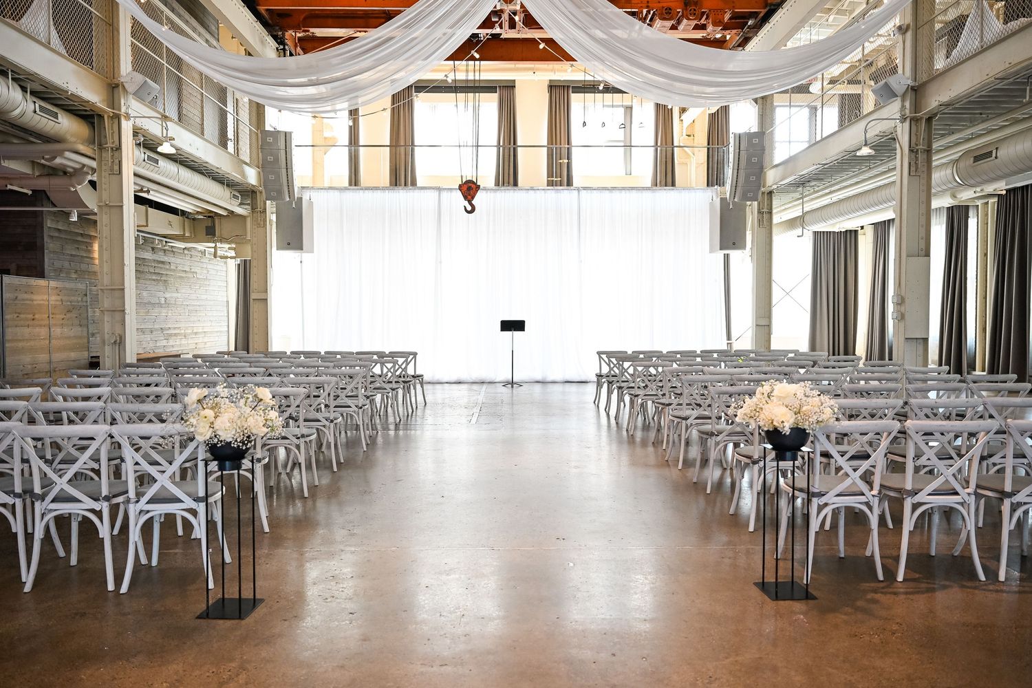Modern wedding venue setup with white chairs and elegant draped ceiling decor.