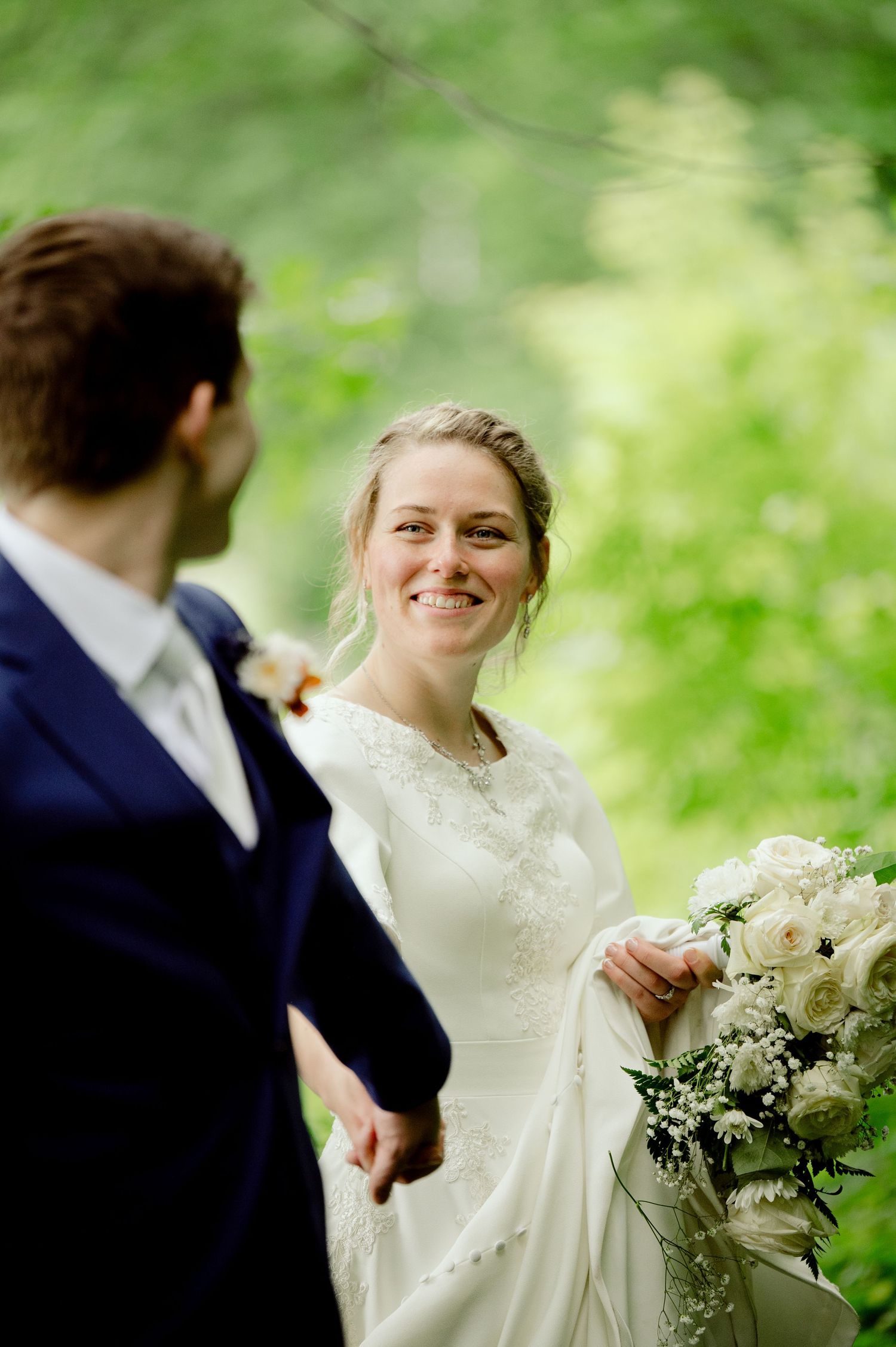 Candid wedding moments captured in a lush green outdoor setting with white floral bouquet.