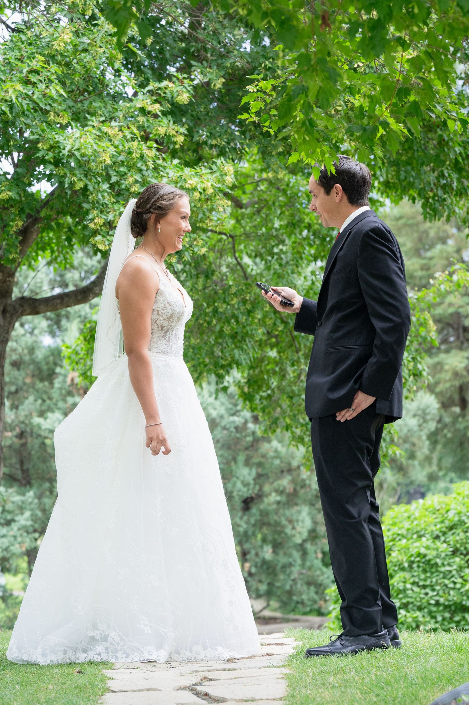 Bride and groom share a romantic first look moment outdoors surrounded by lush green trees.