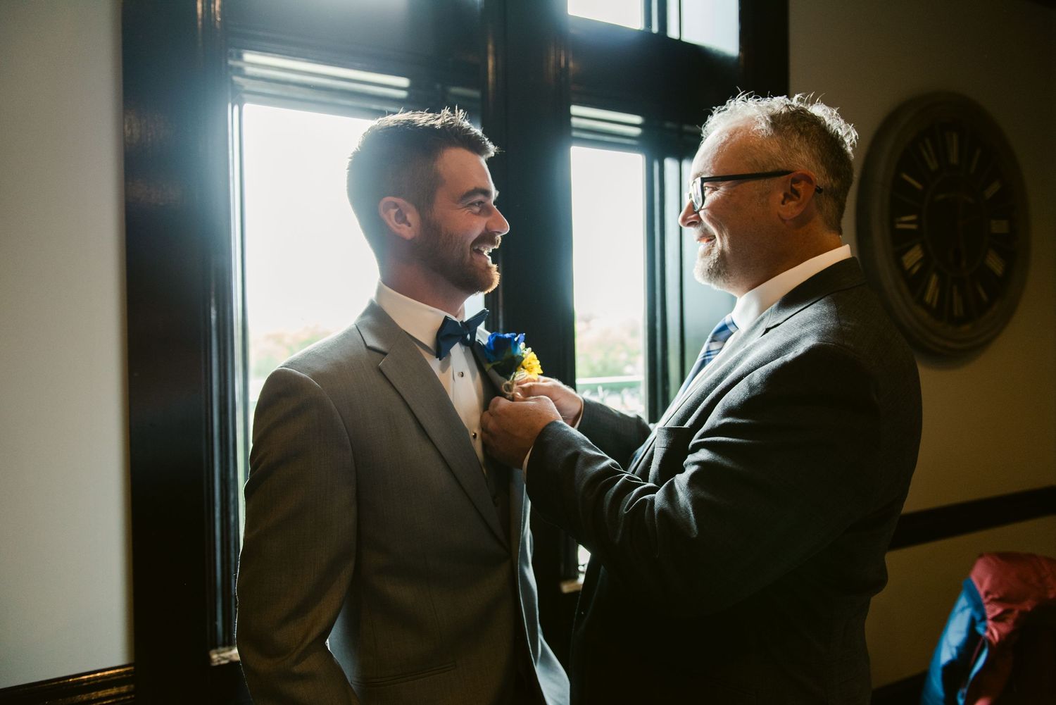 Central MN Wedding Photos | Older man helping groom pin a sunflower boutonniere on his gray suit jacket before the wedding ceremony.