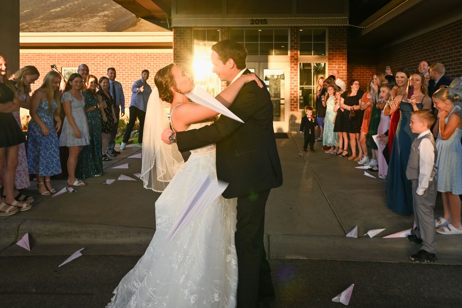 Bride and groom share a kiss during their sparkler send-off exit surrounded by cheering wedding guests at night.