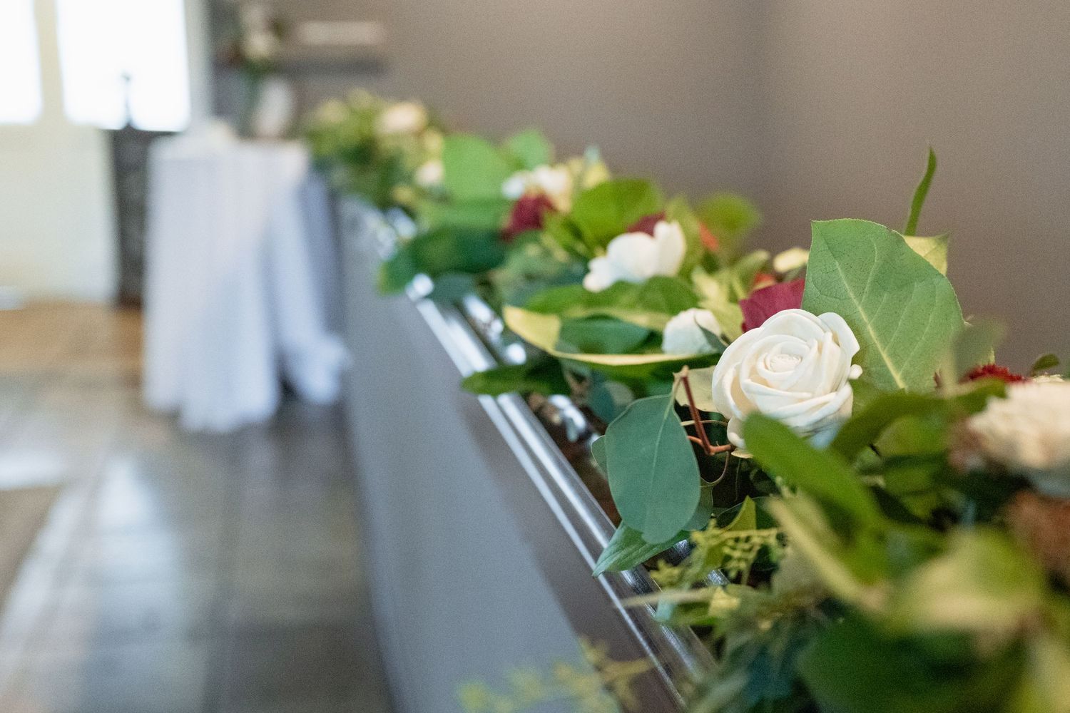 Elegant wedding table garland featuring white roses, red flowers, and lush green leaves as floral decor.