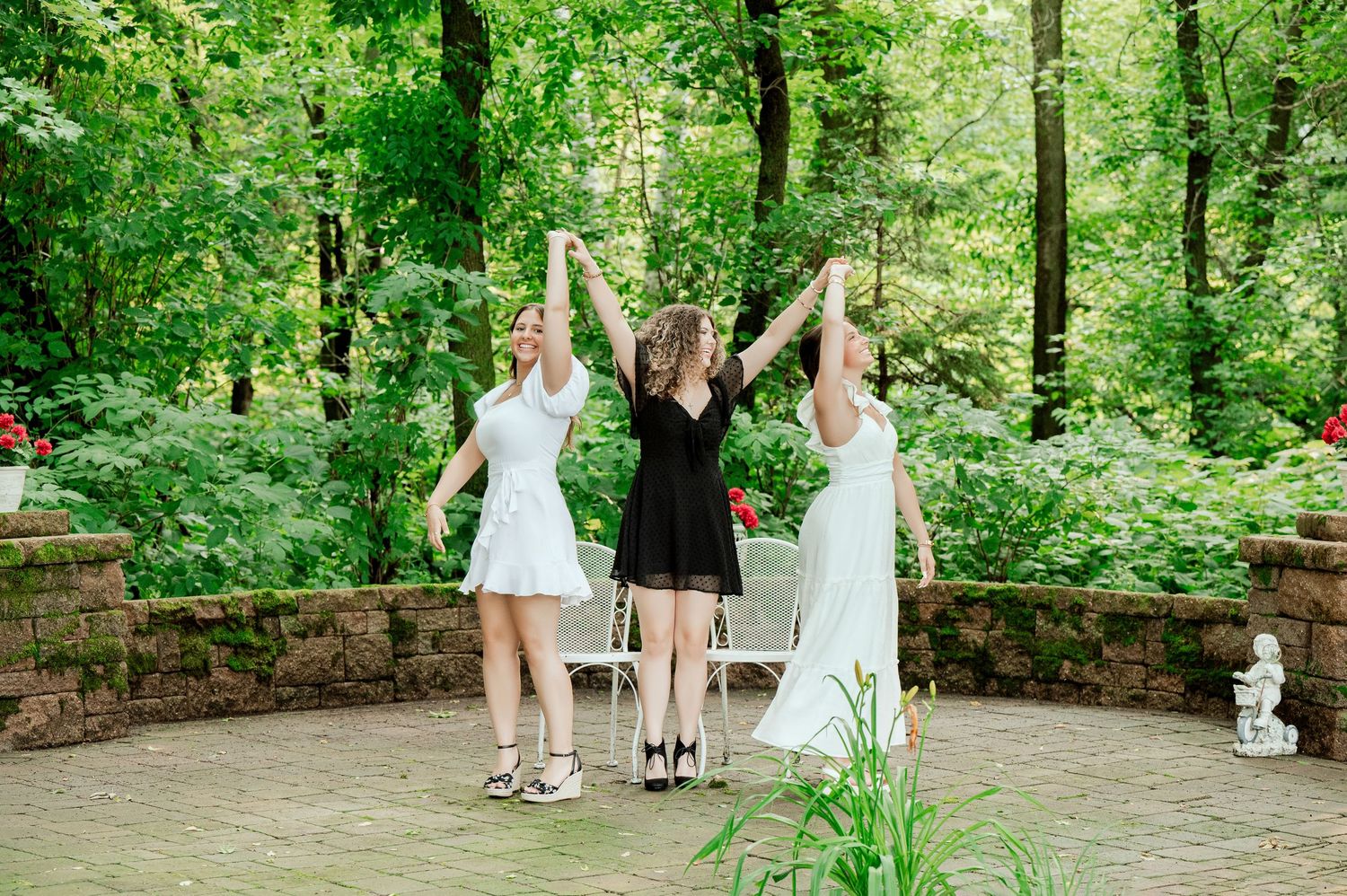 Three friends hold hands and celebrate on stone patio surrounded by green forest.