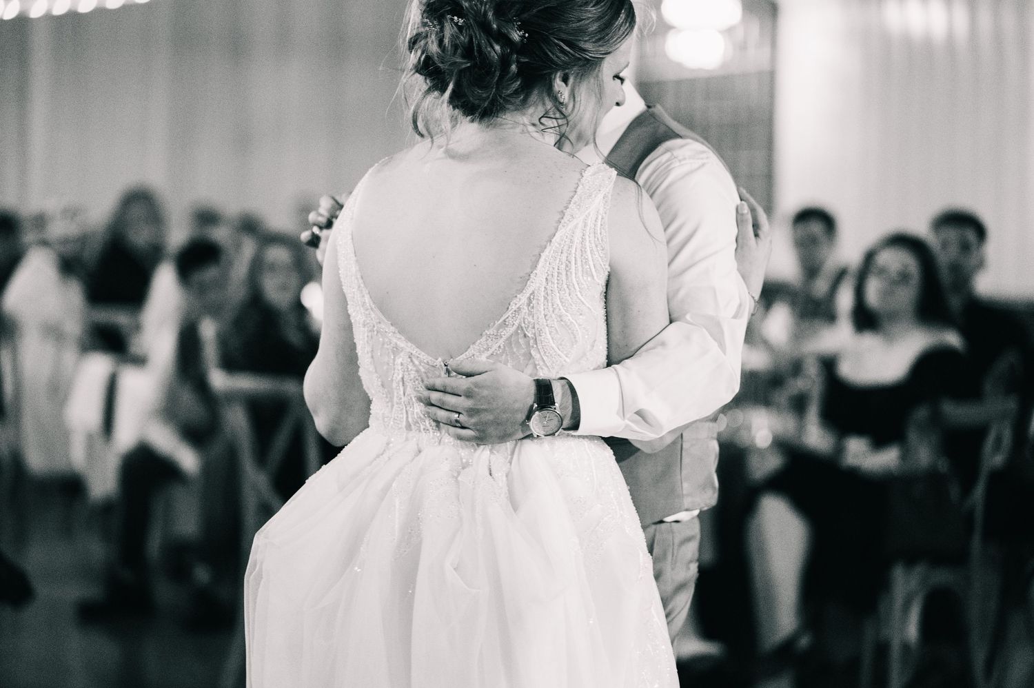 Black and white photo of bride and groom sharing first dance, bride in open-back wedding gown.
