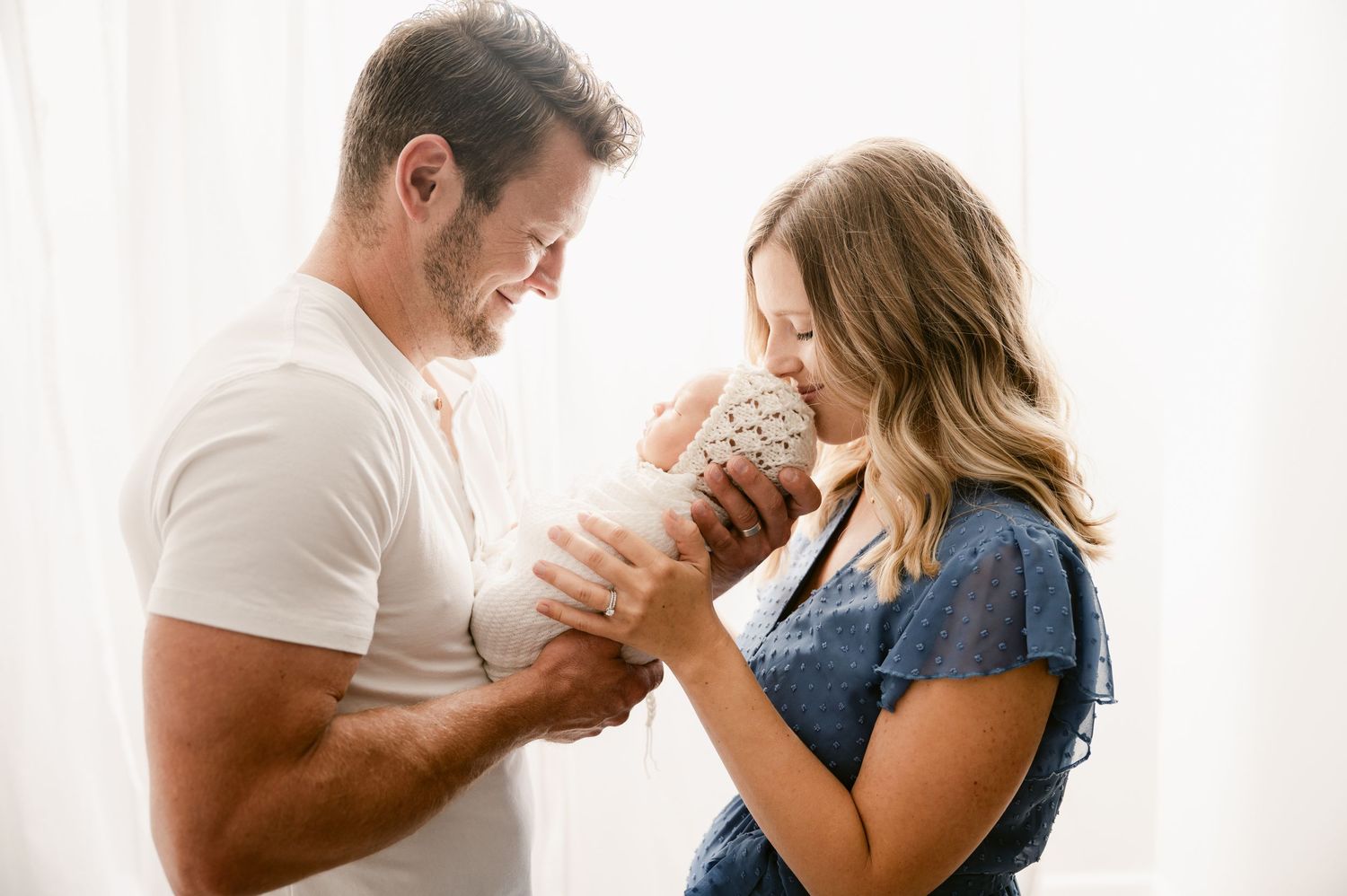 Happy couple smiling at their newborn baby in a bright, airy room during a newborn photography session.